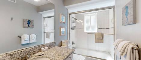 Un baño moderno con lavamanos de granito, inodoro blanco, bañera y ducha con mampara de vidrio.