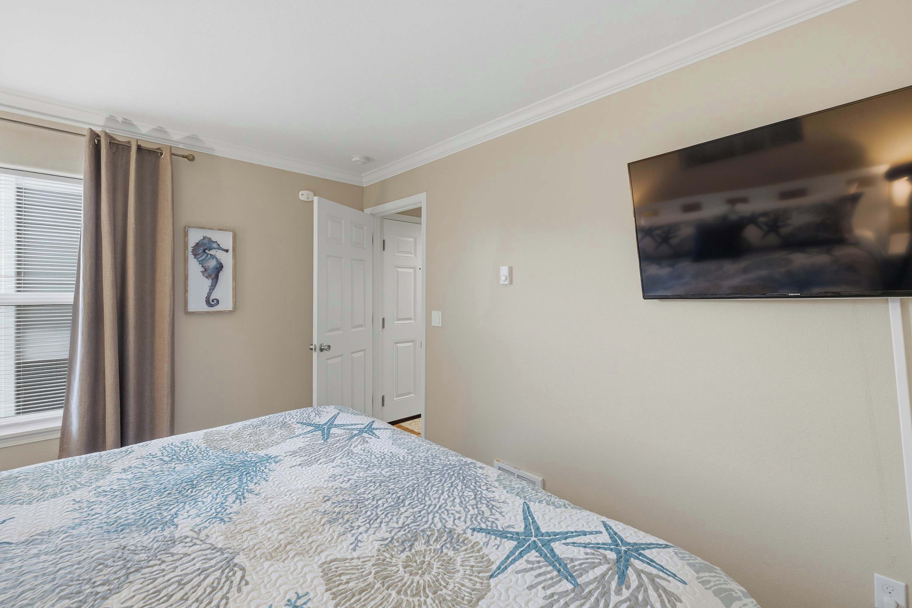 Een slaapkamer met een bed, een aan de muur bevestigde televisie, een deur en een raam met gordijnen.