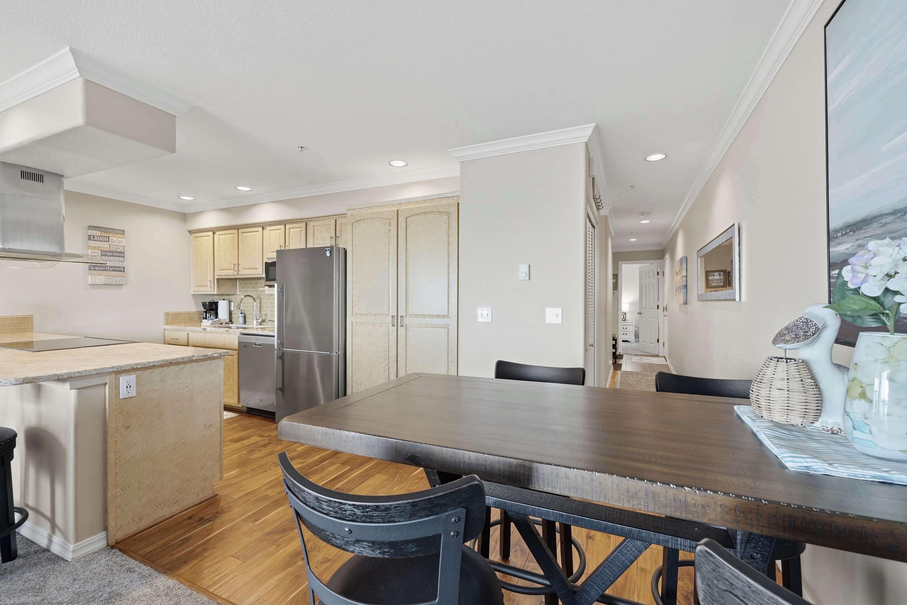 A modern kitchen with wooden cabinets, a central island, and a dining area with a dark wooden table and chairs.