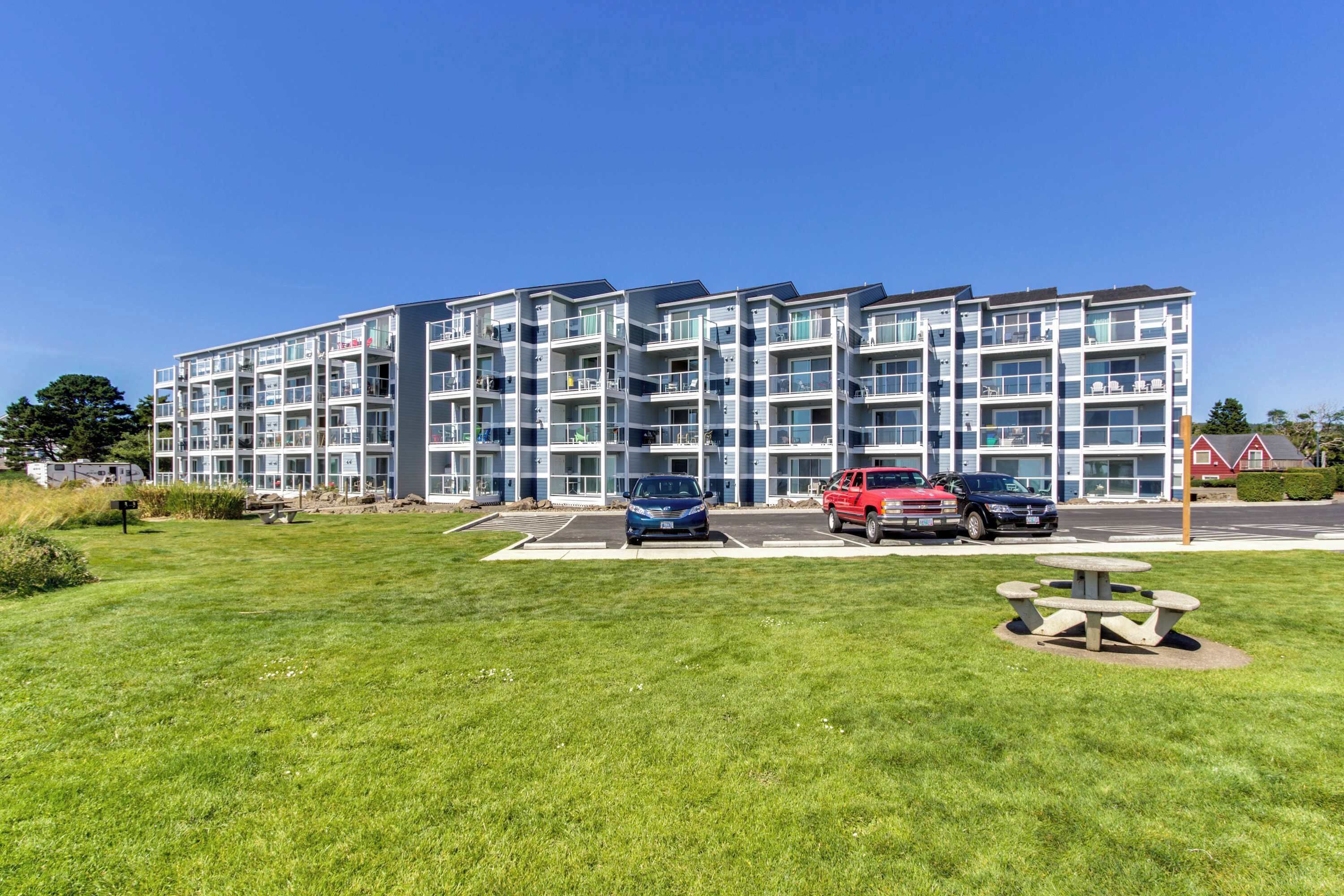 A multi-story residential building with balconies, a parking lot, and a picnic table in the foreground.