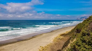A beach with waves, a clear sky, and distant mountains. - Dog friendly home with ocean views hot tub deck foosball and fireplace (Lincoln City)