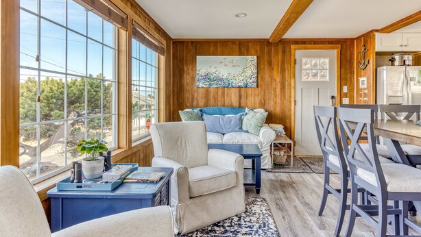 A cozy living room with a large window, a sofa, a coffee table, and a dining area with chairs. - Dog friendly home with ocean views hot tub deck foosball and fireplace (Lincoln City)