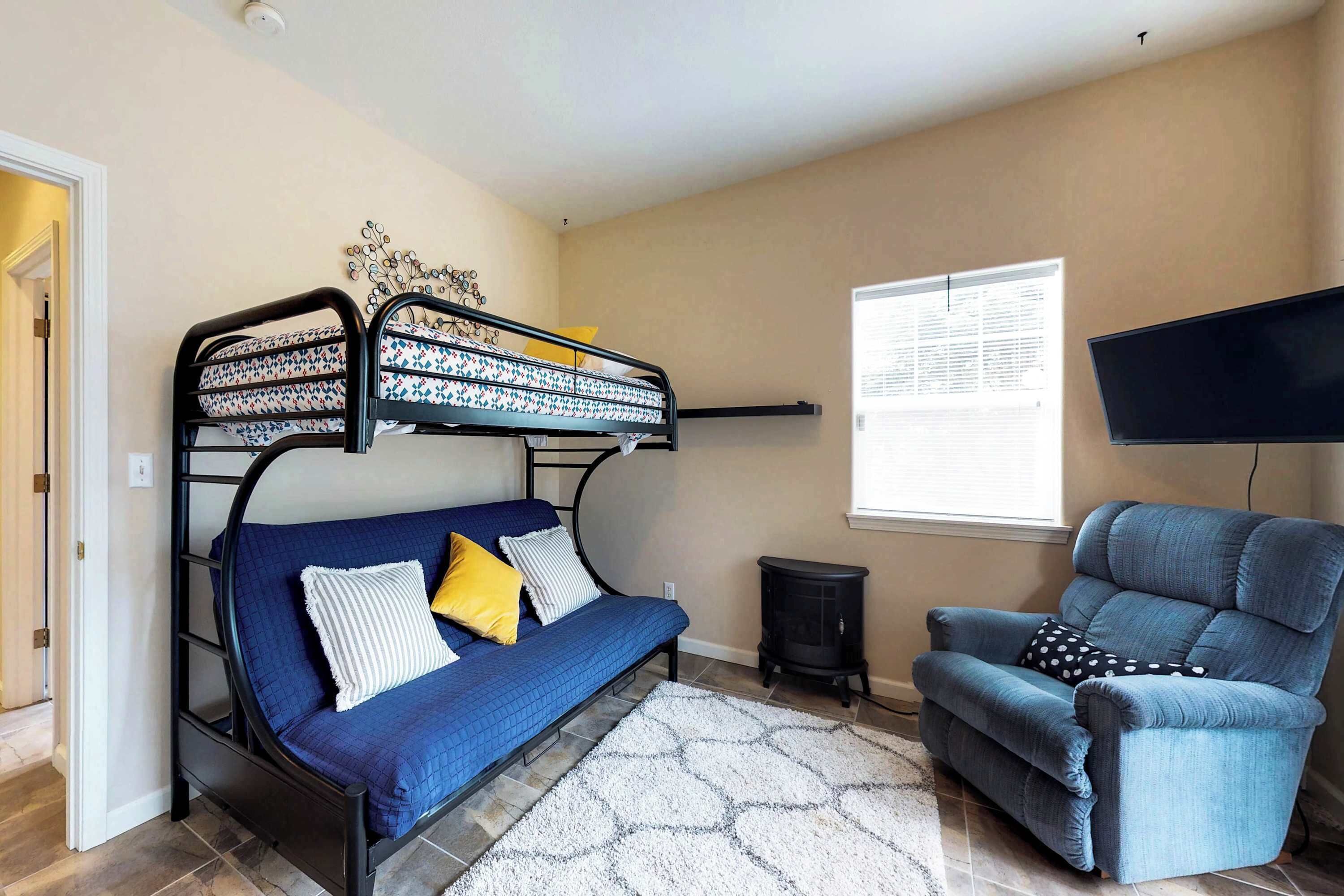 A room with a bunk bed, a sofa, a chair, a TV, and a window.