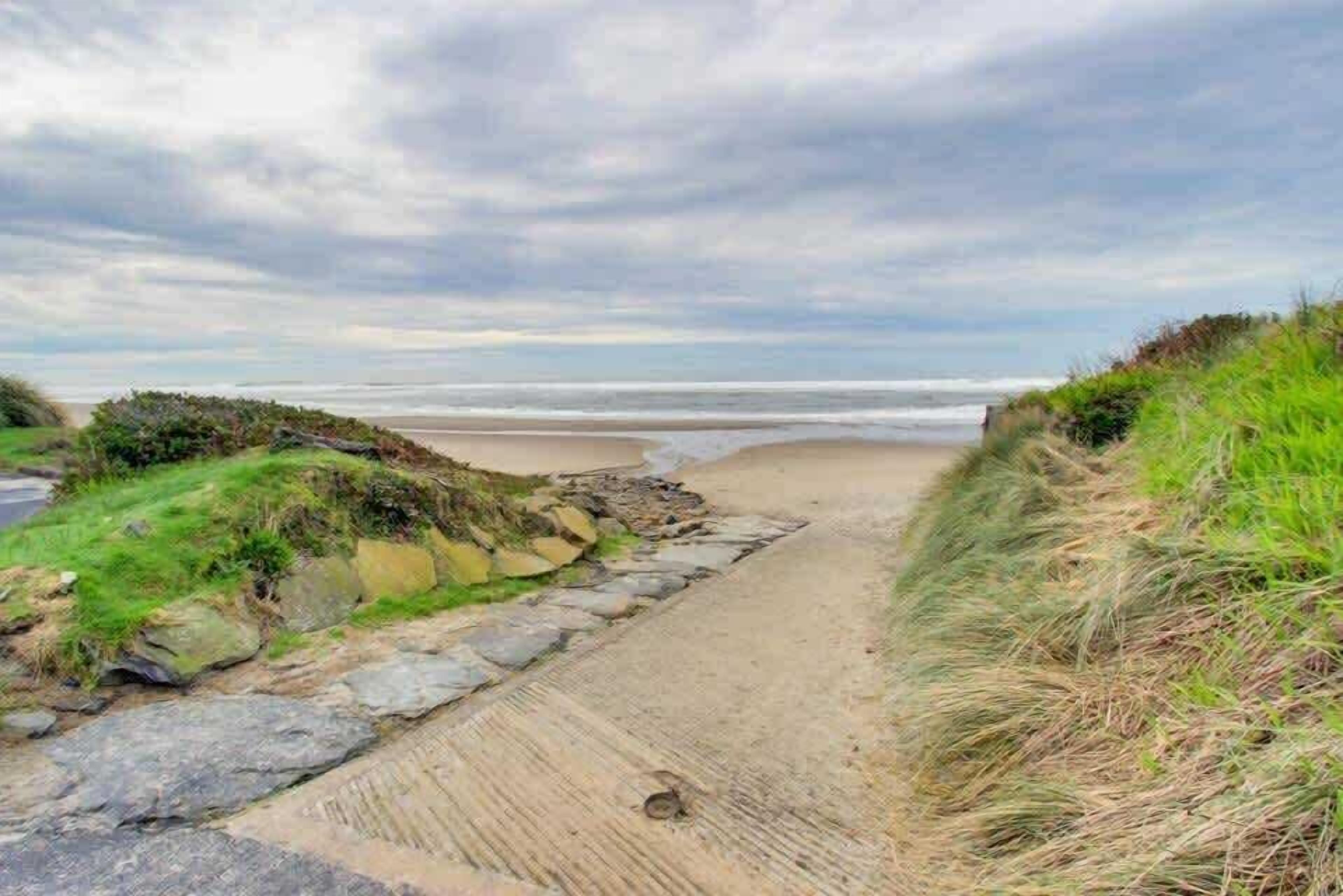A coastal pathway leading to a beach with a rocky and grassy border.