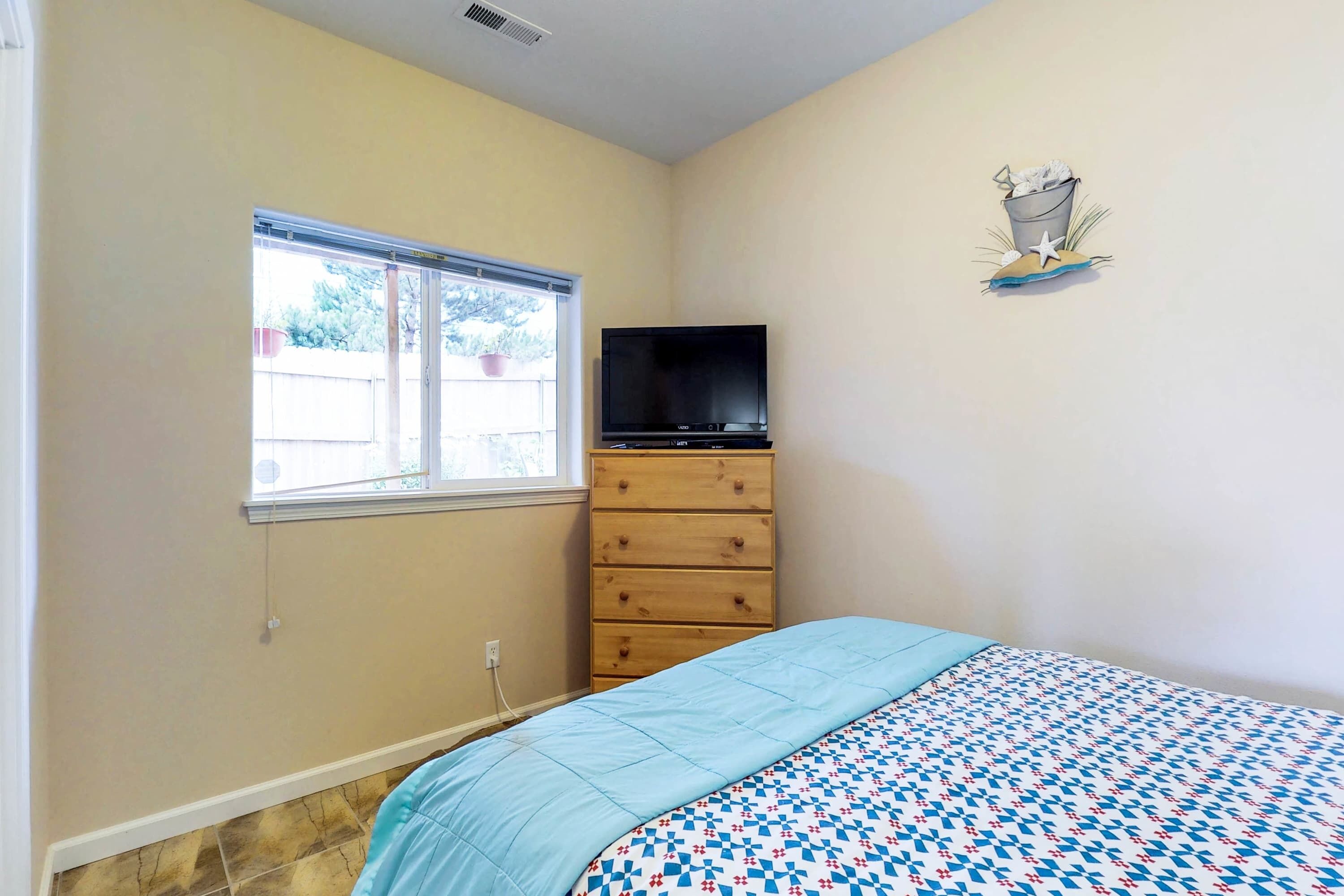 Un dormitorio con cama, cómoda, televisor y ventana.