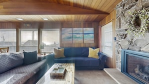 Ein gemütliches Wohnzimmer mit Holzbalkendecke, einem Steinkamin, einem blauen Sofa mit gelben Kissen und einem Couchtisch.
