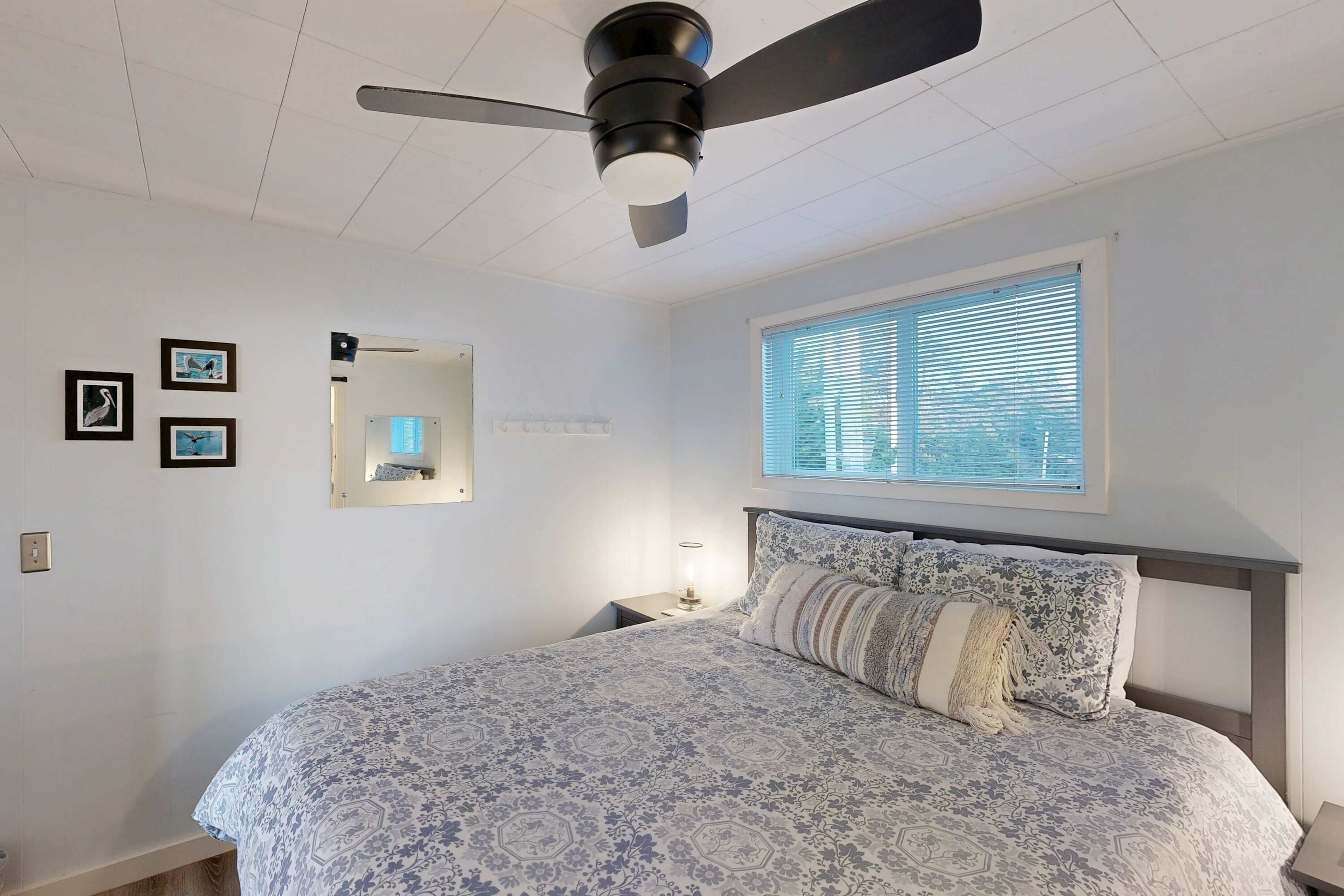 Quarto com cama, ventoinha no teto, janela com persianas e quadros nas paredes.