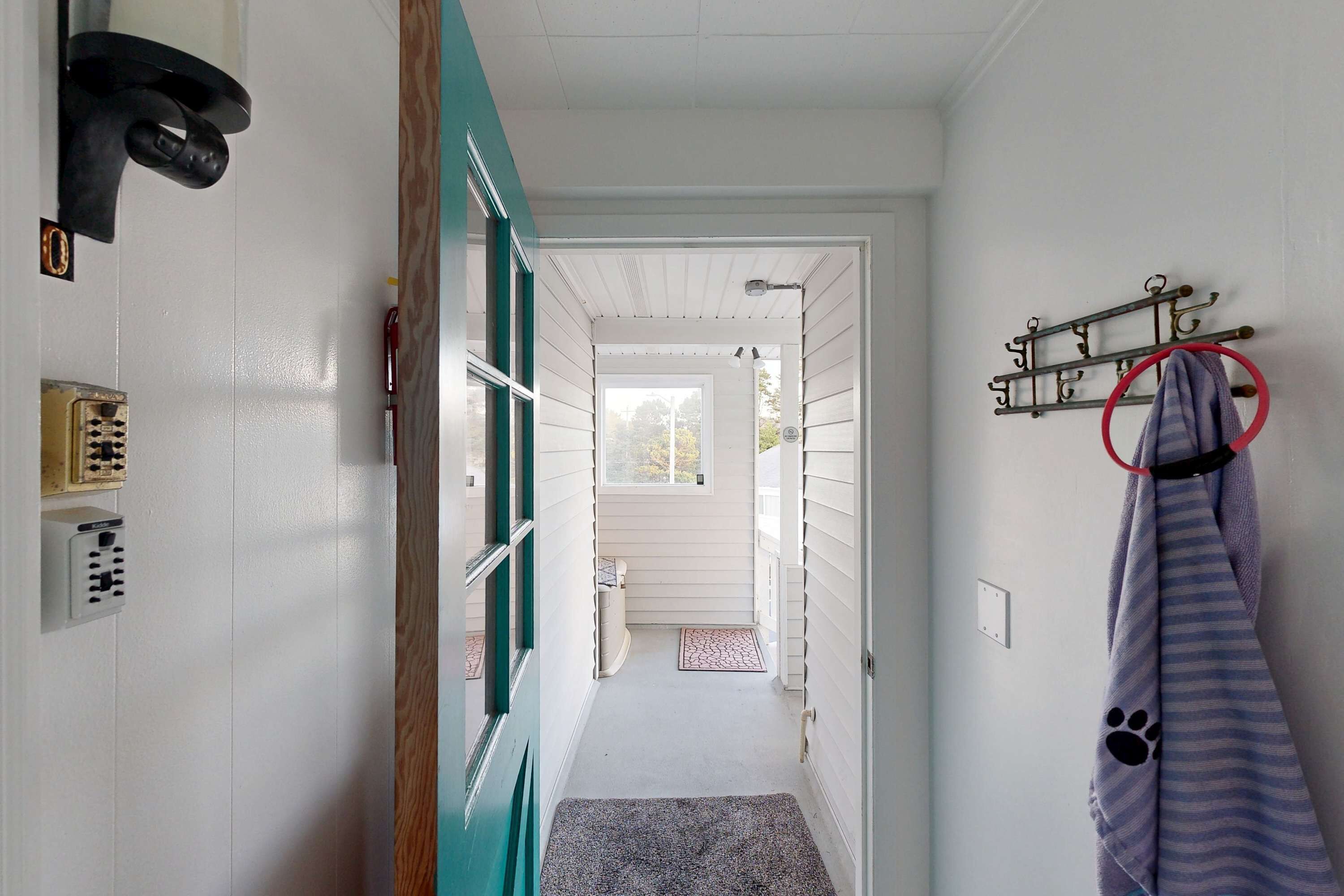 A narrow hallway with a teal door, a pet bed, a coat rack, and a wall-mounted light fixture.
