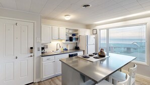 Une cuisine moderne avec des meubles blancs, un îlot central et une vue sur la mer grâce à de grandes fenêtres.