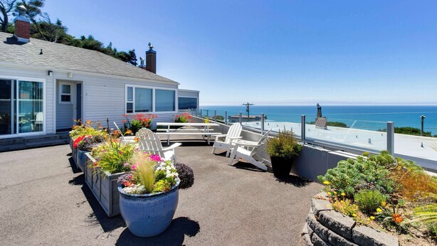 Une terrasse sur le toit, avec des chaises blanches, des plantes en pot et une vue sur l’océan.