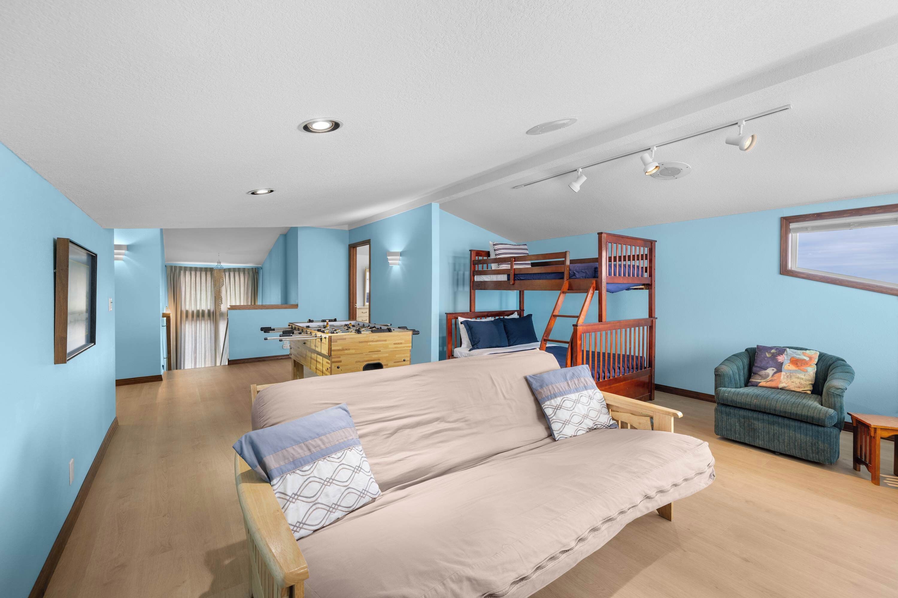 Ein Zimmer mit einem beigen Sofa, einem Holzbett mit Etagen, einem kleinen Sessel und einem Schreibtisch aus Holz mit einem Tischfußballspiel.