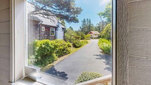 A window view of a residential street with houses, greenery, and a clear sky. - Waterfront house with bay and ocean views large deck and quiet location (Lincoln City)