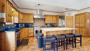 A kitchen with wooden cabinets, a central island with stools, a stove, and a microwave. - Expansive family friendly home with a private hot tub walk to the beach (Lincoln City)