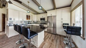 Een moderne keuken met witte kasten, roestvrijstalen apparatuur en een centraal eiland met barkrukken.