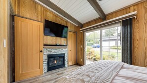 Een slaapkamer met een open haard, houten wanden, een groot raam en een bed met een witte deken.