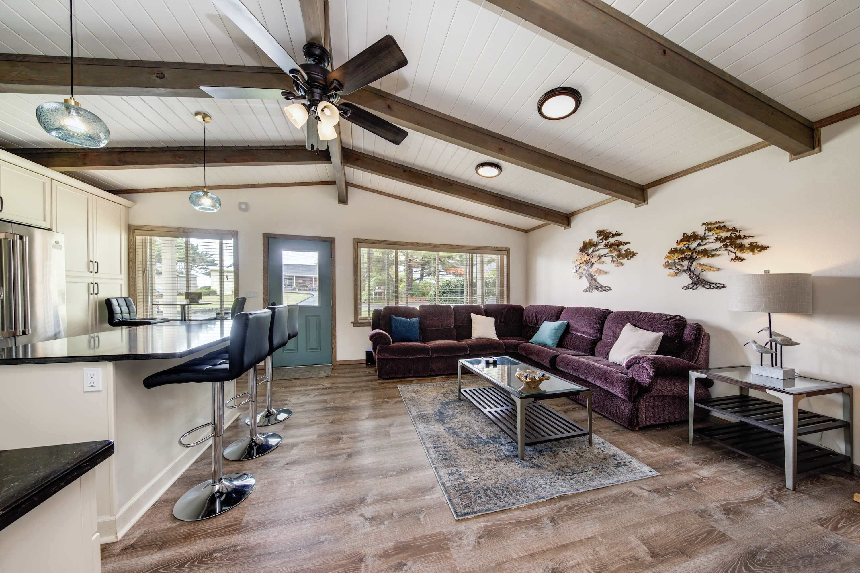 A spacious living area with a wooden ceiling, a sofa set, a coffee table, and a bar area with stools.