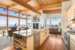A modern kitchen with large windows, a central island, and a view of the ocean. - New home with unparalleled ocean views and private hot tub dogs welcome (Lincoln City)