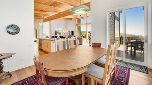 A spacious dining area with a large wooden table and chairs, a modern chandelier, and a view through a sliding glass door to an outdoor patio. - New home with unparalleled ocean views and private hot tub dogs welcome (Lincoln City)