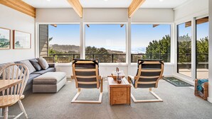 A modern living room with a sofa, two chairs, a coffee table, and large windows offering a view of the outdoors. - New home with unparalleled ocean views and private hot tub dogs welcome (Lincoln City)