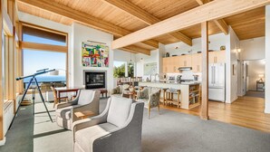 A spacious living area with a fireplace, a dining area, and a kitchen with wooden cabinets and a large refrigerator. - New home with unparalleled ocean views and private hot tub dogs welcome (Lincoln City)