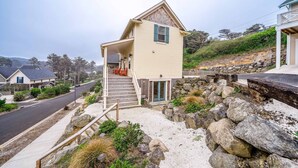 A two-story house with a porch, a stone retaining wall, and a driveway. - Charming three story getaway with two cozy living areas walk to the beach (Lincoln City)