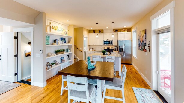 A modern kitchen with white cabinetry, a wooden dining table, and a view to the outside. - Charming three story getaway with two cozy living areas walk to the beach (Lincoln City)