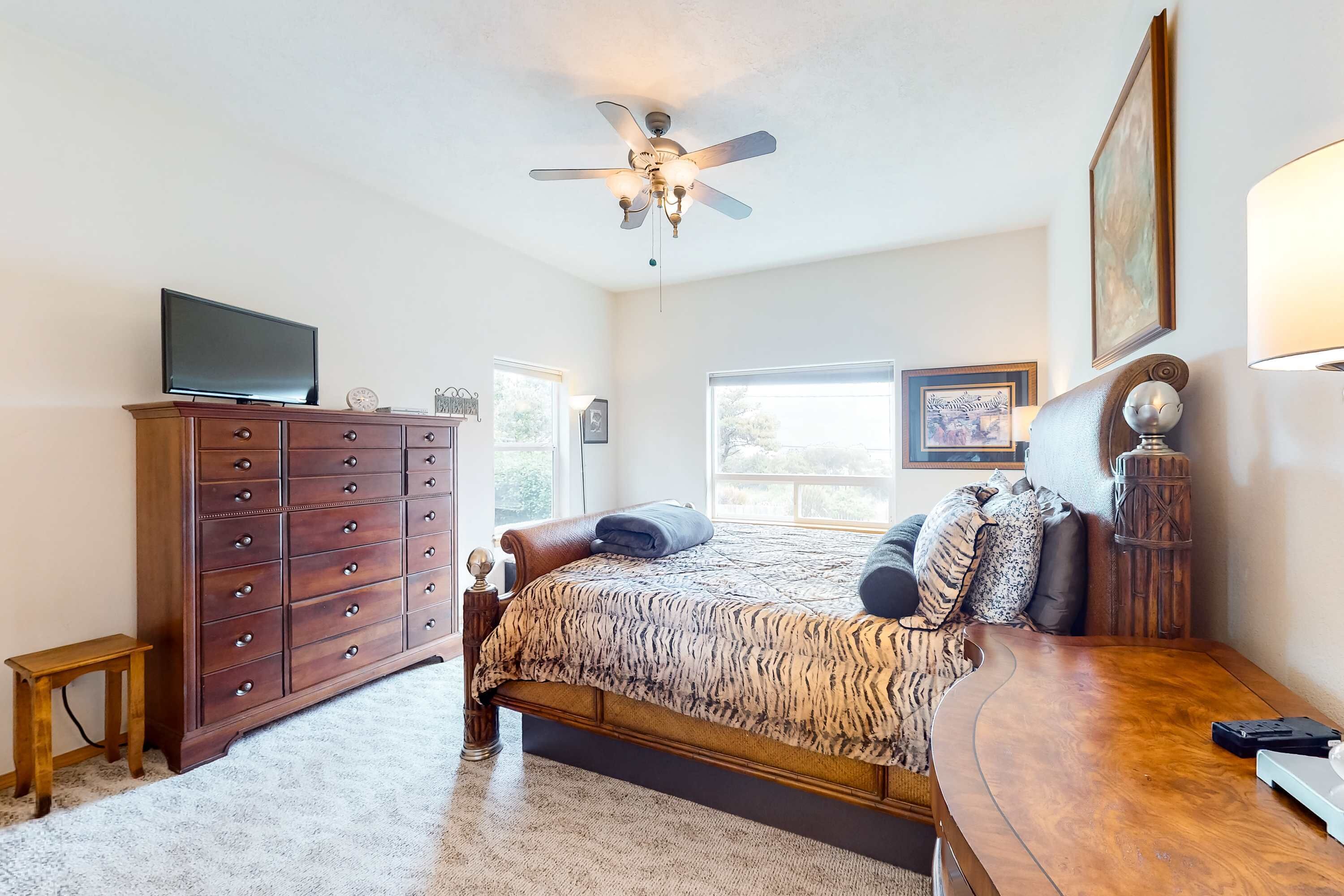 Een slaapkamer met een bed, een dressoir, een televisie en een plafondventilator.