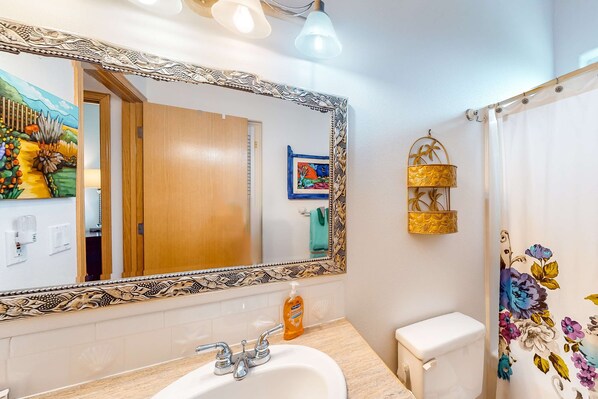 A bathroom with a large mirror, a sink, a toilet, and a shower curtain with a floral pattern. - Comfy beach home with ocean views free WiFi private washer dryer and deck (Lincoln City)