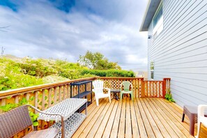 A wooden deck with outdoor furniture, including a table and chairs, and a view of a landscaped garden. - Comfy beach home with ocean views free WiFi private washer dryer and deck (Lincoln City)