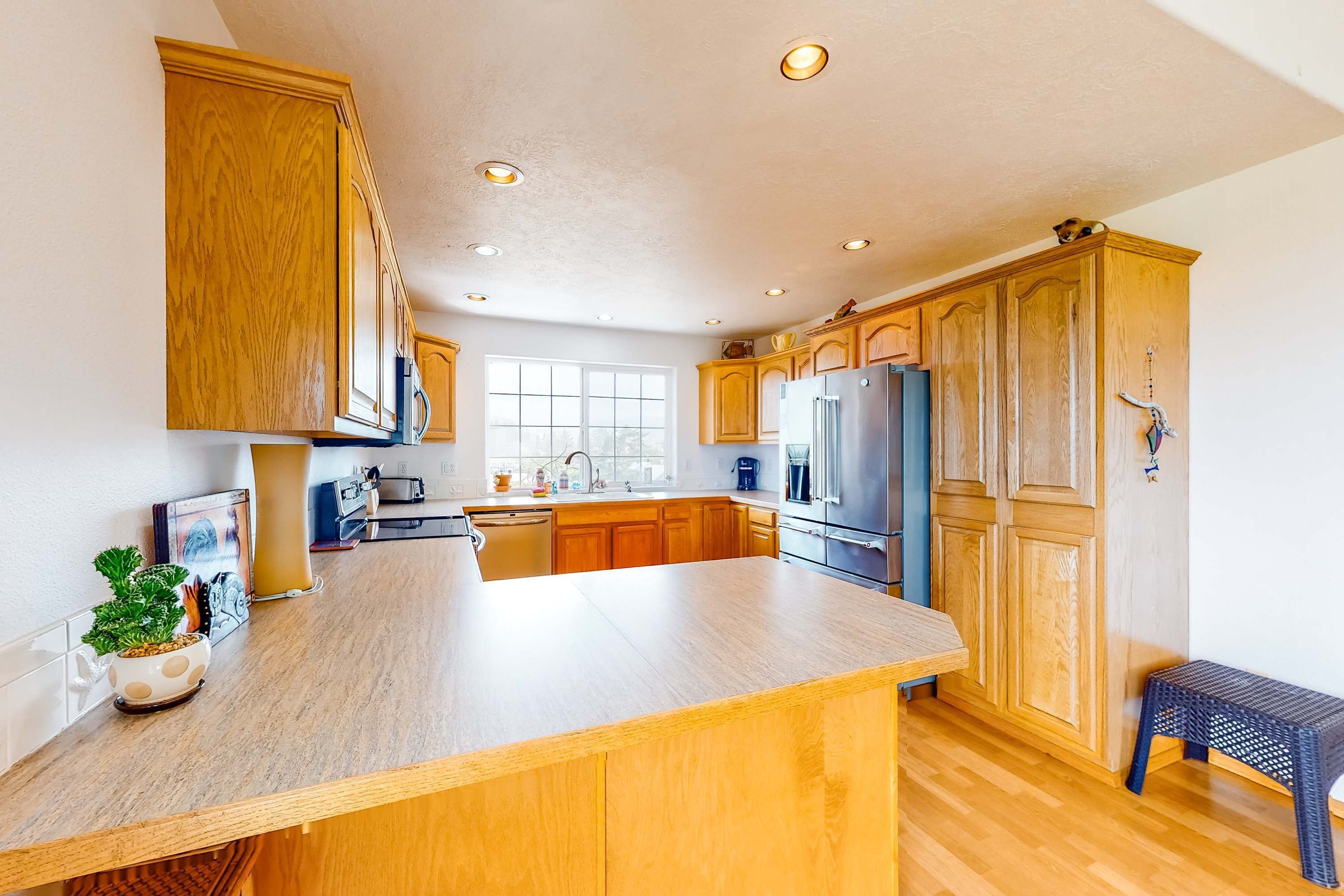 Een keuken met houten kastjes, een groot eiland, een koelkast en een raam dat voor natuurlijk licht zorgt.