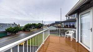 Een balkon met een houten terras, een witte reling en een witte plastic stoel.