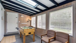 Een kamer met een wand van hout, een deur, een tafelvoetbalspel, een stoel en grote ramen met zonwering.