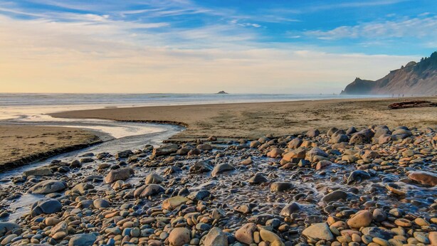 Een rotsachtig strand met een heldere lucht en verre landschapselementen.