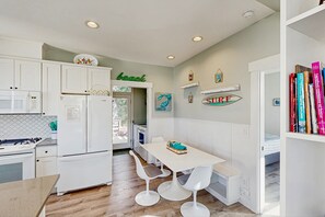 Une cuisine moderne avec des meubles blancs, un coin repas comprenant une table et des tabourets de bar, et une bibliothèque remplie de livres.