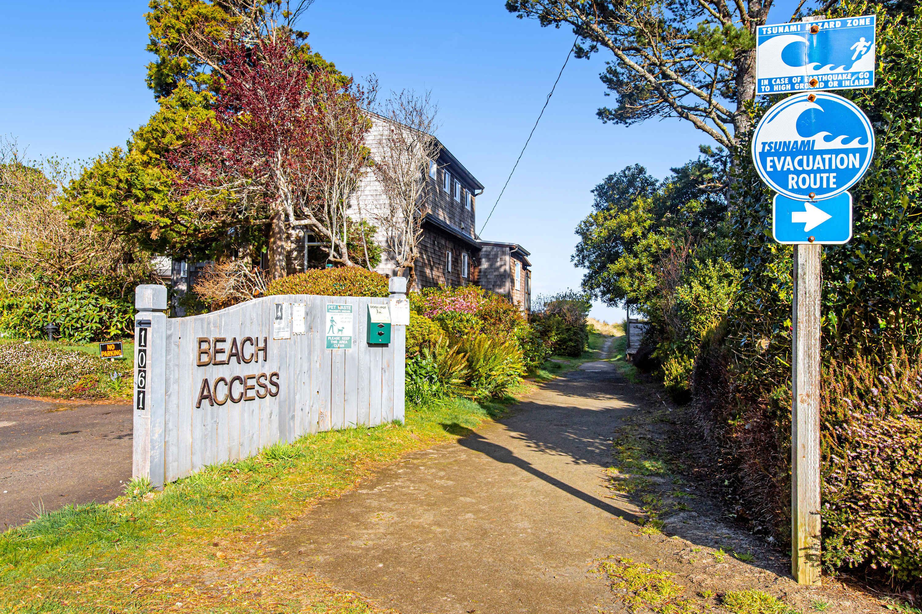 A beach access sign, a tsunami evacuation route sign, and a house with a wooden exterior.