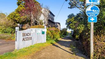 A beach access sign, a tsunami evacuation route sign, and a house with a wooden exterior.