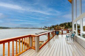 Une terrasse en bois avec une balustrade donnant sur une étendue d’eau, un banc et une vue sur un quartier résidentiel.