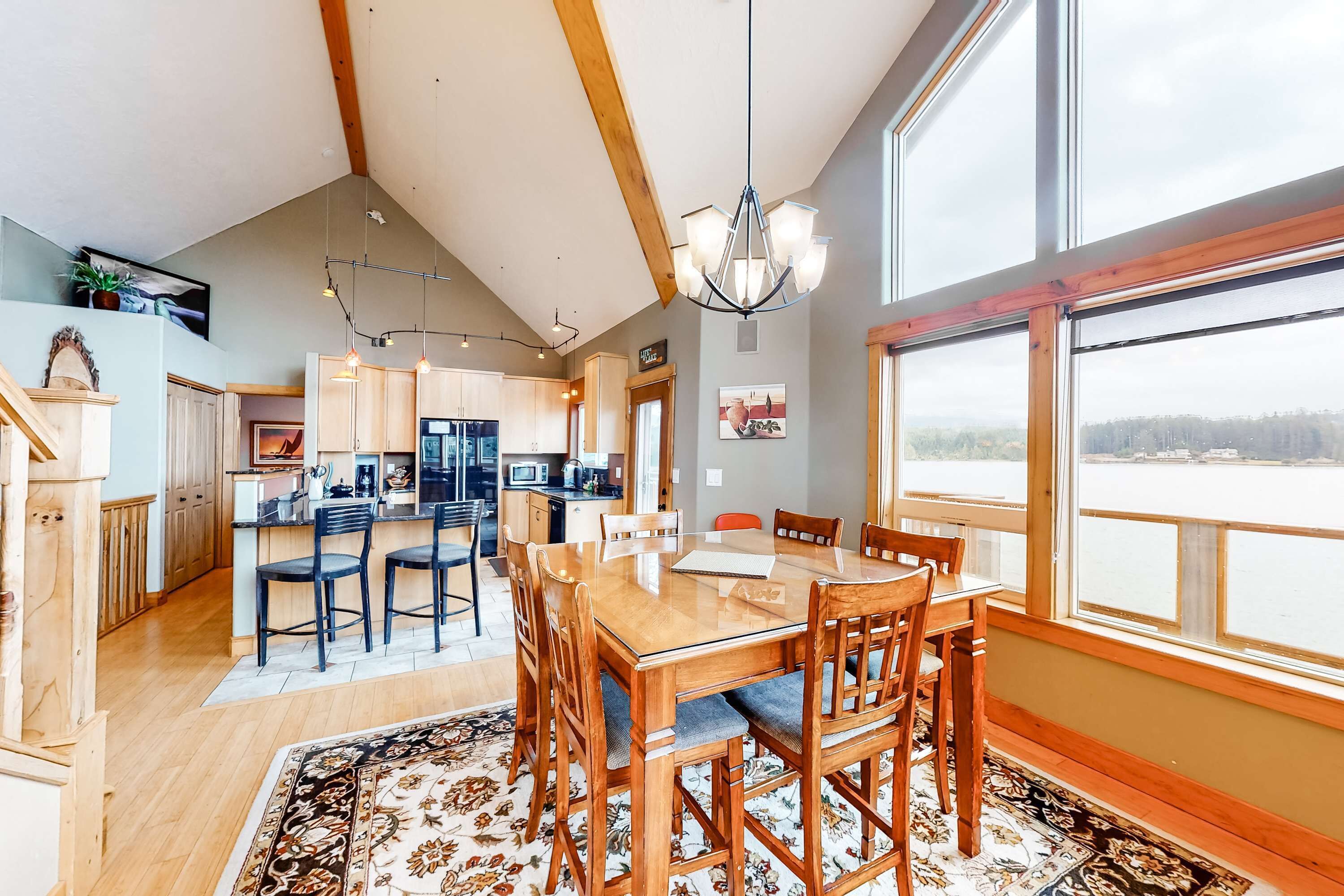 A spacious kitchen with wooden cabinets, a dining table with chairs, and large windows offering a view of a body of water.