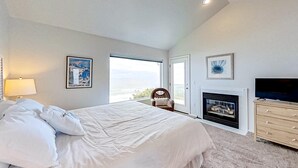 Un dormitorio con una cama grande, chimenea, televisor y vistas al exterior.