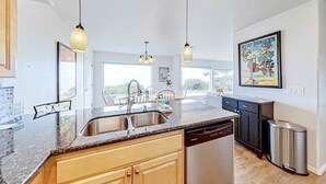 Una cocina moderna con una isla central, pileta de acero inoxidable e iluminación colgante.