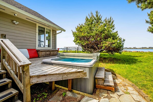 A hot tub in a backyard with a wooden deck, a staircase, and a view of the water. - Dog Friendly Bayfront Beauty with a Private Hot Tub Free WiFi and Washer Dryer (Lincoln City)