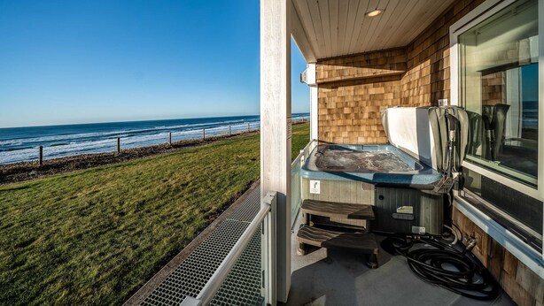 A balcony with a hot tub, overlooking a grassy area and the ocean. - Oceanfront condo with private hot tub ocean views and high speed WiFi (Lincoln City)