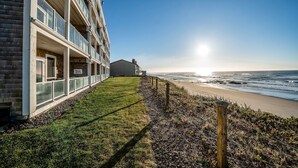 A beachfront hotel with a grassy lawn, a wooden fence, and a view of the ocean. - Oceanfront condo with private hot tub ocean views and high speed WiFi (Lincoln City)