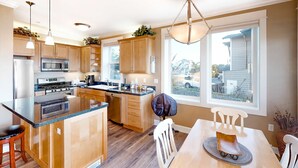 A modern kitchen with wooden cabinets, a central island, stainless steel appliances, pendant lighting, and a view of the outside through large windows. - Oceanfront condo with private hot tub ocean views and high speed WiFi (Lincoln City)