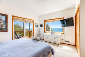 Quarto com cama, televisão, cômoda e varanda com vista para o mar.