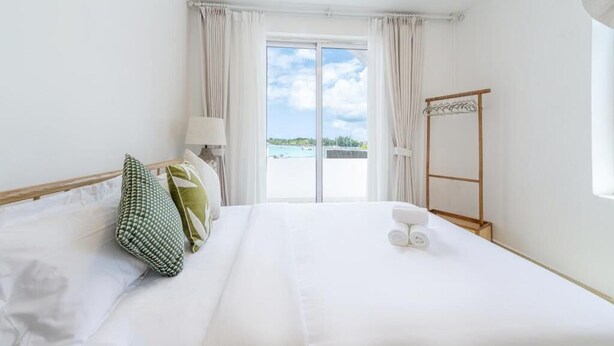 Une chambre d’hôtel avec un lit, une fenêtre avec des rideaux, un porte-vêtements en bois et une vue sur l’extérieur.