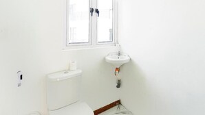 Une petite salle de bain blanche, avec des toilettes, un lavabo et une fenêtre.