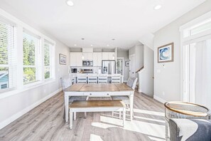 Une cuisine moderne avec des meubles blancs, un îlot central et un coin repas comprenant une table et des chaises en bois.