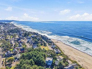 Una vista aerea di una zona residenziale lungo la costa, con case affacciate sulla spiaggia, cielo sereno e l'oceano sullo sfondo.