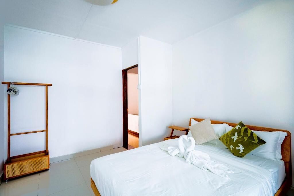 Una cama bien hecha con sábanas blancas y un almohadón verde, una mesita de noche de madera y un armario de madera.